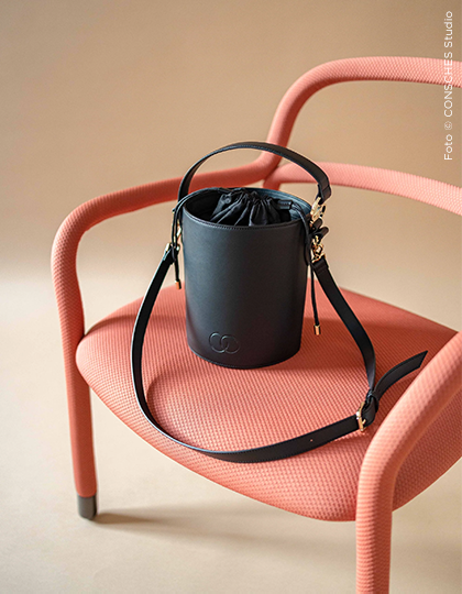 Schwarze Bucket Bag von CONSCHES auf rosa Designerstuhl – nachhaltige Handtasche mit elegantem Look