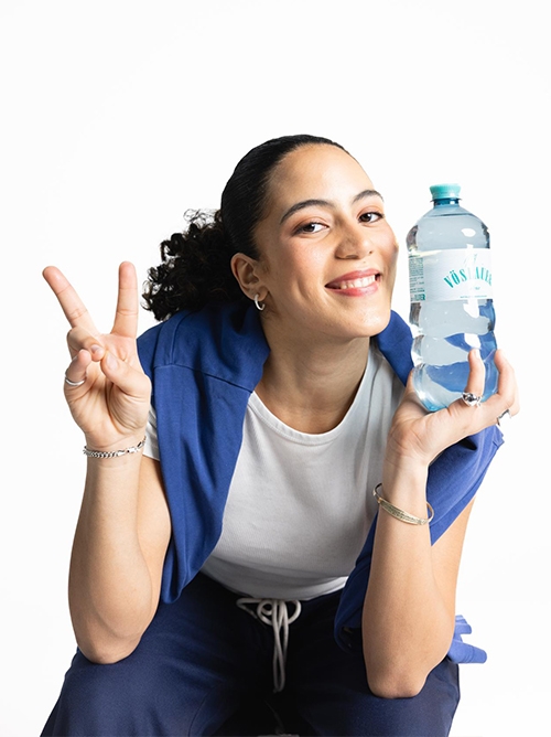 Nő egy Vöslauer Flavours Orange Passion Plus üvegpalackot tart feje fölött.